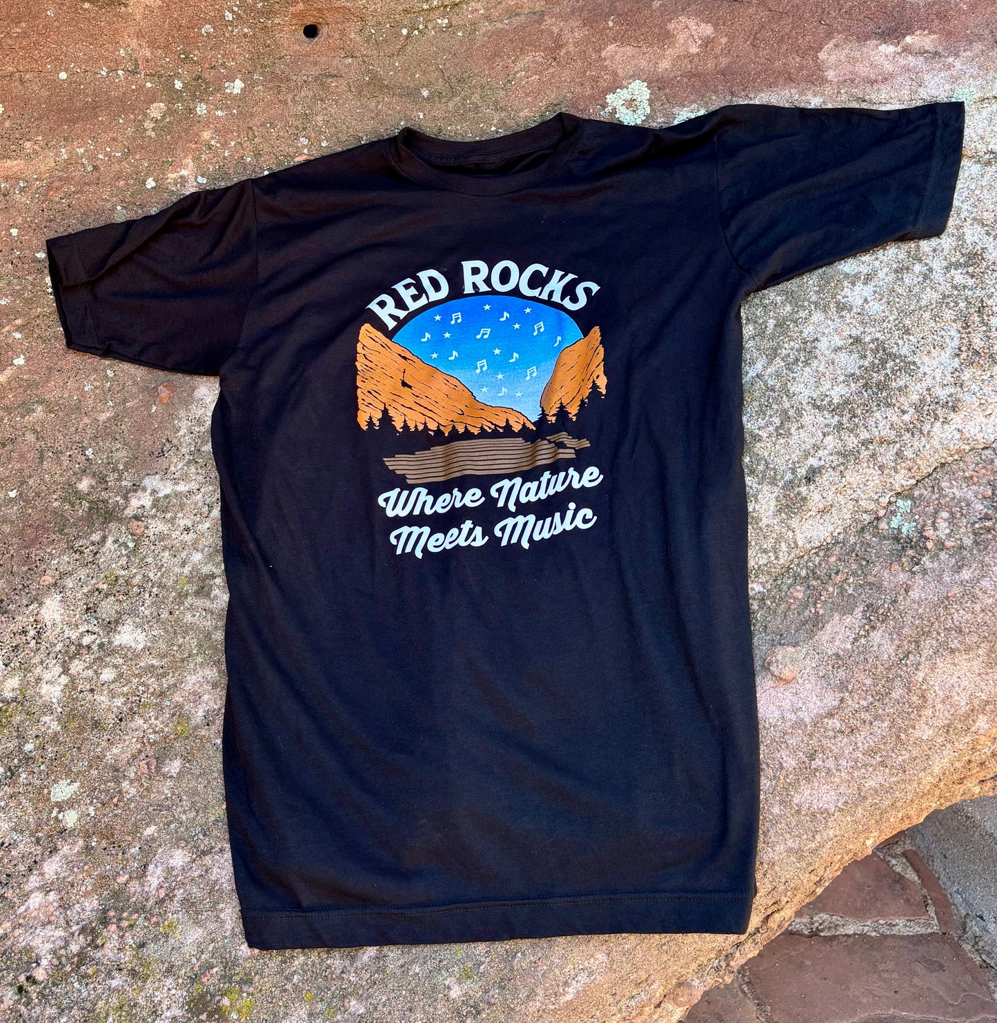 Black t-shirt with 'Red Rocks Where Nature Meets Music' graphic on a stone surface
